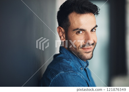 Portrait of confident and casual man leaning against a grey wall looking happy, proud and glad while smiling. Face of stylish, handsome and young european male standing alone inside with copy space 121876349