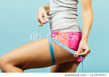 Fitness woman measuring her thigh on blue Fitness woman measuring her thigh on blue 121876457