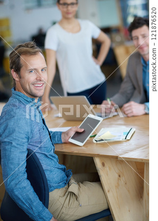 Smiling marketing manager browsing the internet on a digital tablet in an office. Handsome and happy professional researching creative ideas to promote and advertise a startup on social media 121876520