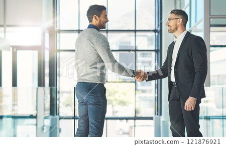 Businessman standing, smiling and with a handshake, greets a colleague in an office. Executive meets client or partner and shakes hands. Two happy professionals agree on a successful business project 121876921