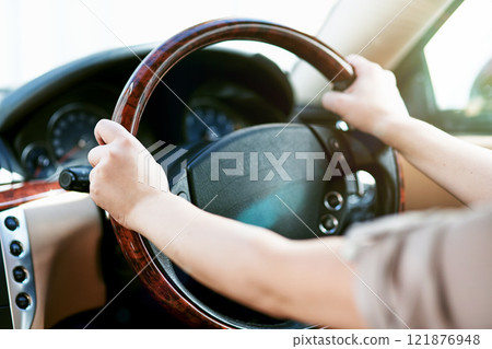 Hands of a driver on a steering wheel in a car for travel, driving or taking a roadtrip. Take a drive in a taxi, cab or with a rideshare service. Closeup of a limousine chauffeur practicing safety 121876948