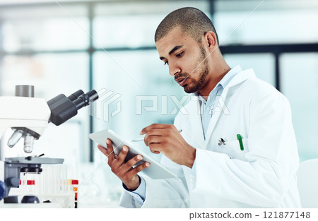 Serious male scientist working on a tablet reviewing an online phd publication in a lab. Laboratory worker updating health data for a science journal. Medical professional document clinical trial 121877148