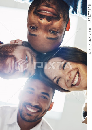 Portrait of a diverse group of happy office workers from below joining together in a huddle for support and unity with lights in the background. Cheerful motivated colleagues ready for business 121877166