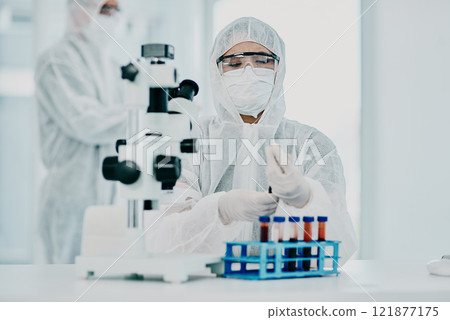A scientist conducting a medical experiment to research covid vaccine in a lab and collecting blood samples. Healthcare researcher analyzing chemicals in a chemistry laboratory wearing a hazmat suit 121877175