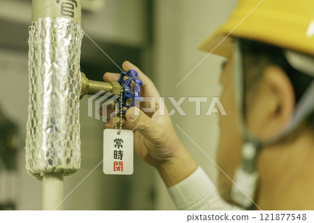 Close-up of a male worker's hands closing a valve. Photo courtesy of Denpa Gakuen, Tokyo Electronics College. 121877548