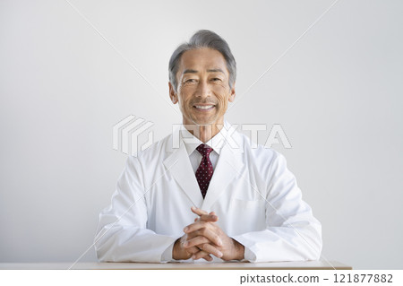 A man in his 60s wearing a white coat and smiling at the camera 121877882
