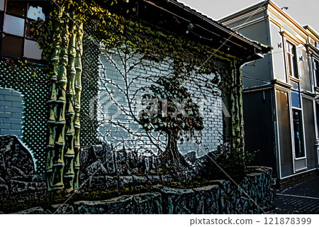 Beautifully decorated wall of the house. The wall design combines decorative elements in the form of a tree and natural climbing ivy. Beautifully decorated wall of the house. The wall design combines decorative elements in the form of a tree and natural climbing ivy. 121878399