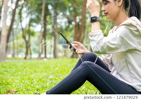 Young woman sitting and listening to music at the park. 121879029