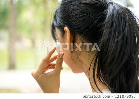 Young woman sitting and listening to music at the park. 121879053