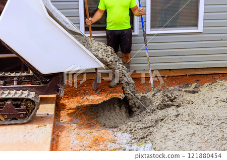 Construction worker uses shovel to spread concrete poured from wheelbarrow truck for new foundation 121880454