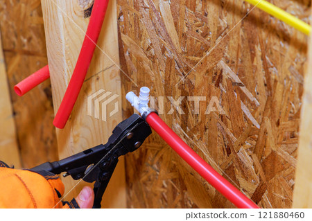 Worker applies pressure with crimping tool to secure red tubing against an oriented strand board wall in workshop. 121880460