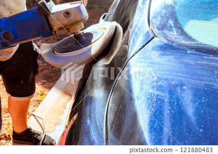 Worker is buffing blue car with power tool, aiming for shiny finish at car service shop 121880483