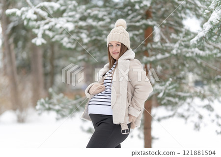 Young pregnant woman in a snowy winter forest looking at the camera with copy space. Expecting mother smiling, looking at her belly outdoors, natural light. Concept of maternity and joy of pregnancy Young pregnant woman in a snowy winter forest looking at the camera with copy space. Expecting mother smiling, looking at her belly outdoors, natural light. Concept of maternity and joy of pregnancy 121881504