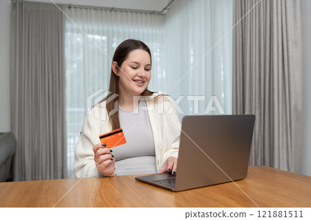 Smiling pregnant woman shopping online with a credit card and laptop at home with copy space for text. Concept of convenience, ecommerce, and preparing for motherhood through digital shopping. Smiling pregnant woman shopping online with a credit card and laptop at home with copy space for text. Concept of convenience, ecommerce, and preparing for motherhood through digital shopping. 121881511