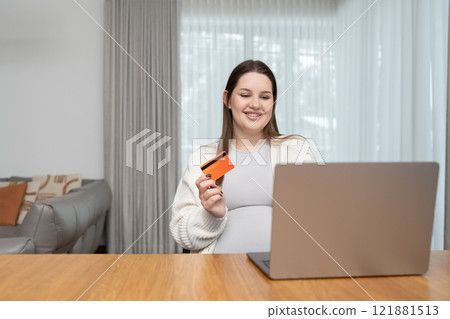 A joyful pregnant woman using her laptop and credit card for online shopping at home, copy space. Concept of preparing for motherhood, ecommerce and embracing technology in everyday life A joyful pregnant woman using her laptop and credit card for online shopping at home, copy space. Concept of preparing for motherhood, ecommerce and embracing technology in everyday life 121881513