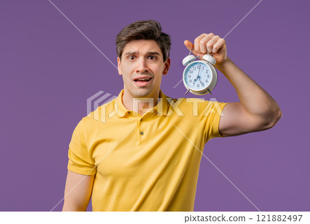 Woken up by alarm clock sleepy handsome man holding it in hand.violet background 121882497