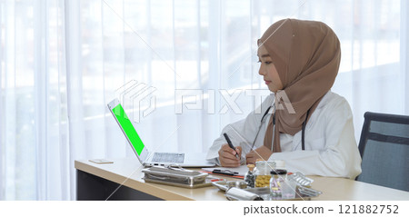 Beautiful young muslim woman doctor smile and looking at camera holding pen and taking notes in hospital office, Medicine and health care concept. 121882752