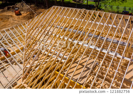 Workers are busy assembling wooden roof beams at construction site, creating framework of new building. 121882756