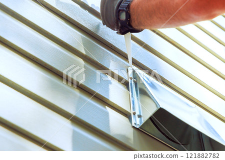Worker is applying sealant around metal vent cover on house siding for better ventilation to prevent leaks. 121882782