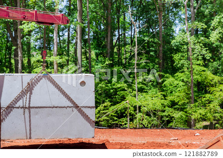 Crane lifts concrete septic tank onto construction site surrounded by lush green trees during construction new home Crane lifts concrete septic tank onto construction site surrounded by lush green trees during construction new home 121882789