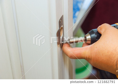 Close up of hand tightening screw into door latch plate during home maintenance tasks. Close up of hand tightening screw into door latch plate during home maintenance tasks. 121882791