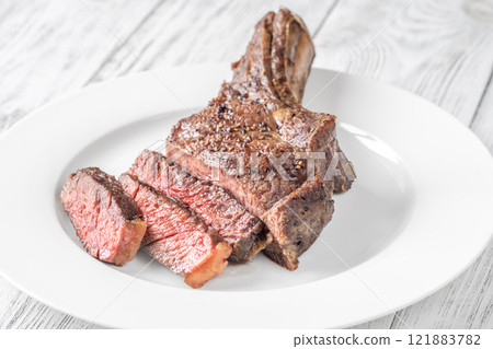 Sliced Grilled Medium-Rare Cowboy Steak on White Plate and Table 121883782