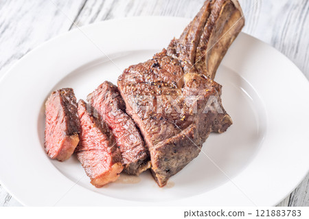 Sliced Grilled Medium-Rare Cowboy Steak on White Plate and Table 121883783