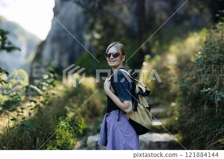 Ojcowski park. Portrait of a happy 30s hiker female standing on the slope of mountain ridge against mountains. woman is happy and looking at camera.  121884144