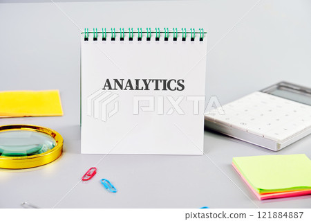 A spiral notebook displays the word analytics, surrounded by office supplies essential for data analysis and project organization A spiral notebook displays the word analytics, surrounded by office supplies essential for data analysis and project organization 121884887