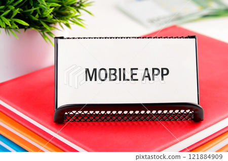 Display of mobile app signage on a vibrant stack of notebooks in a bright office environment 121884909