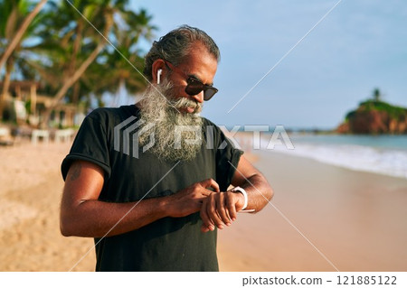Senior classy man with gray beard in sunglasses uses smart watch on beach. Tech-savvy grandpa tracks fitness. Stylish old bearded man enjoys modern gadget lifestyle. Active mature on ocean shore. Senior classy man with gray beard in sunglasses uses smart watch on beach. Tech-savvy grandpa tracks fitness. Stylish old bearded man enjoys modern gadget lifestyle. Active mature on ocean shore. 121885122