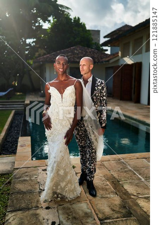 Gender fluid person in white dress with LGBTQ groom in suit near pool at tropical wedding. Celebrate love, diversity in exotic setting. Perfect for gay weddings, travel, inclusive events. 121885147