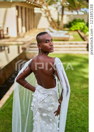 Ambiguous gender fluid person in elegant white gown at villa. LGBTQ wedding scene. Modern bridal fashion. Tropical garden setting. Inclusive love celebration. 121885188
