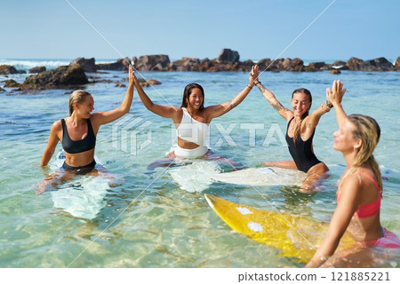 Four women surfers high-five in ocean waves. Celebrate friendship, adventure. Beach setting, sunny day. Empowerment, unity, joy. Surfboards inspire female athleticism. Water, rocks, sun, happiness. Four women surfers high-five in ocean waves. Celebrate friendship, adventure. Beach setting, sunny day. Empowerment, unity, joy. Surfboards inspire female athleticism. Water, rocks, sun, happiness. 121885221