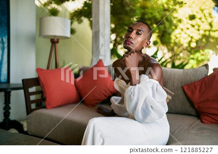 Ambiguous gender fluid person in white bridal dress sits on villa couch. Modern LGBTQ wedding, unique style fashion. Tropical background. Celebrating diversity, love. 121885227