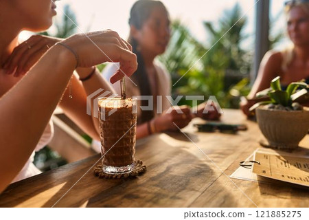 Group of friends relax in outdoor cafe with iced coffee drinks. Sunlit patio with rich plants. People chat, enjoy beverages. Casual meeting or social gathering. Group of friends relax in outdoor cafe with iced coffee drinks. Sunlit patio with rich plants. People chat, enjoy beverages. Casual meeting or social gathering. 121885275