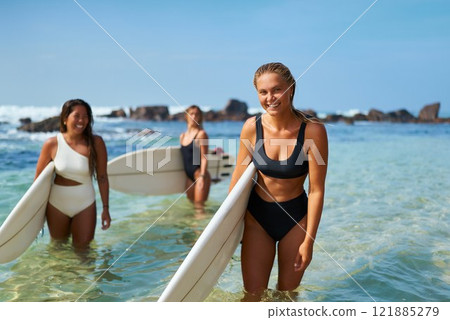 Three fit women with surfboards smile at sunny beach. Female surfers enjoy water sports at ocean shore. Active lifestyle by sea, healthy outdoor activity. Girls wear swimwear, prepare to surf waves. Three fit women with surfboards smile at sunny beach. Female surfers enjoy water sports at ocean shore. Active lifestyle by sea, healthy outdoor activity. Girls wear swimwear, prepare to surf waves. 121885279