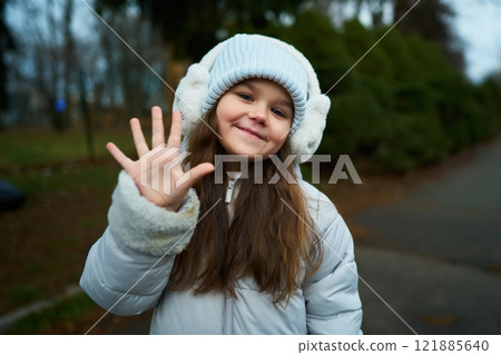 Young girl happily waving her hand in a winter park setting Young girl happily waving her hand in a winter park setting 121885640