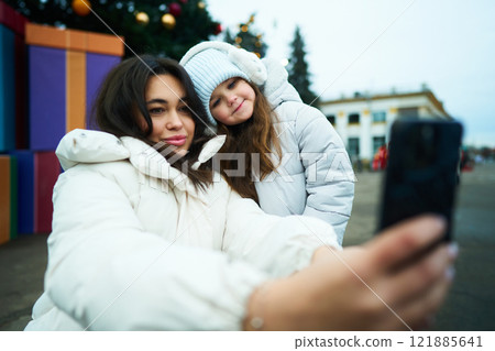 Smiling girls taking a selfie outdoors during winter festivities Smiling girls taking a selfie outdoors during winter festivities 121885641