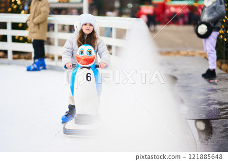 Child enjoying an ice skating experience with a penguin-shaped skating aid 121885648
