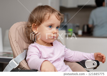 A calm toddler seated in a highchair observing the home surroundings with curiosity. 121885775