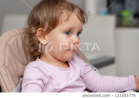 A thoughtful toddler seated in a highchair observing their surroundings with quiet curiosity. 121885776