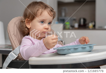 A toddler in a highchair carefully exploring their food in a calm home setting. A toddler in a highchair carefully exploring their food in a calm home setting. 121885778