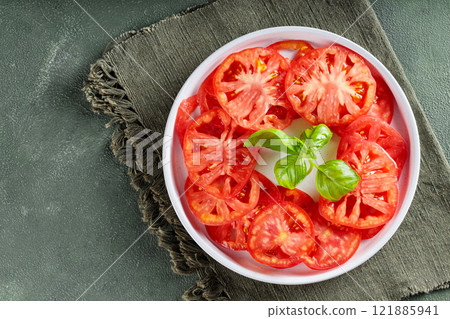 Red Tomato Slices and Fresh Basil Leaves on White Plate with Green Linen Napkin, Copy Space 121885941