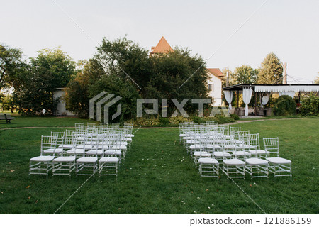 A row of pristine white chairs is neatly lined up in a grassy field A row of pristine white chairs is neatly lined up in a grassy field 121886159
