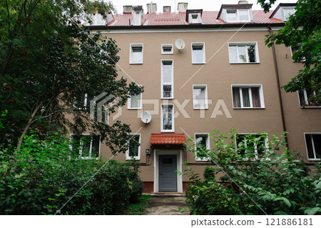 A tall building featuring numerous windows and greenery in front of it A tall building featuring numerous windows and greenery in front of it 121886181