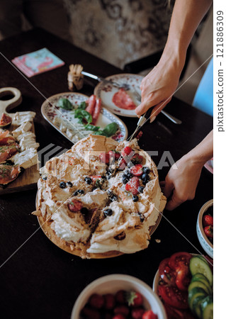 A person is cutting a cake topped with strawberries and blueberries 121886309