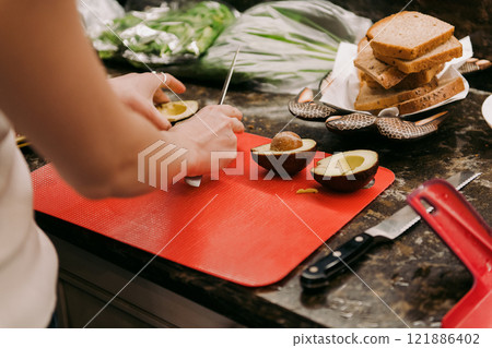 A woman is skillfully cutting fresh avocados on a vibrant red cutting board A woman is skillfully cutting fresh avocados on a vibrant red cutting board 121886402