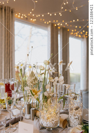 A wedding reception table set with flowers in vases and glasses 121886421