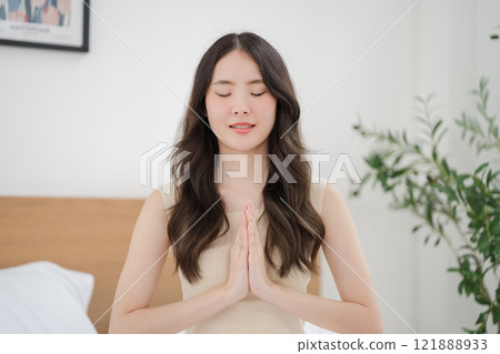 Asian woman doing a yoga pose with hands clasped on the bed 121888933